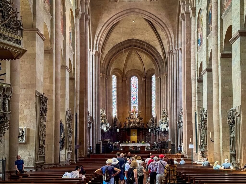 A tour group gathers in the nave of a Gothic church, admiring the high vaulted ceilings and stained glass. Visitors explore the detailed stone arches and pillars within the sacred space.