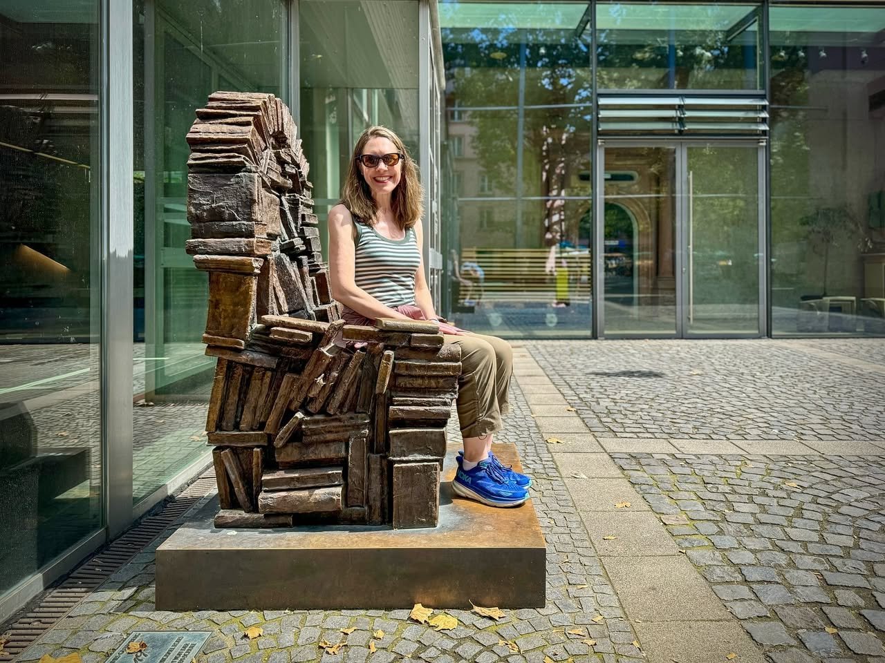 Gutenberg-Museum Mainz A person sits on a rusted armchair sculpture outside a building. The background features glass panels and pavement.