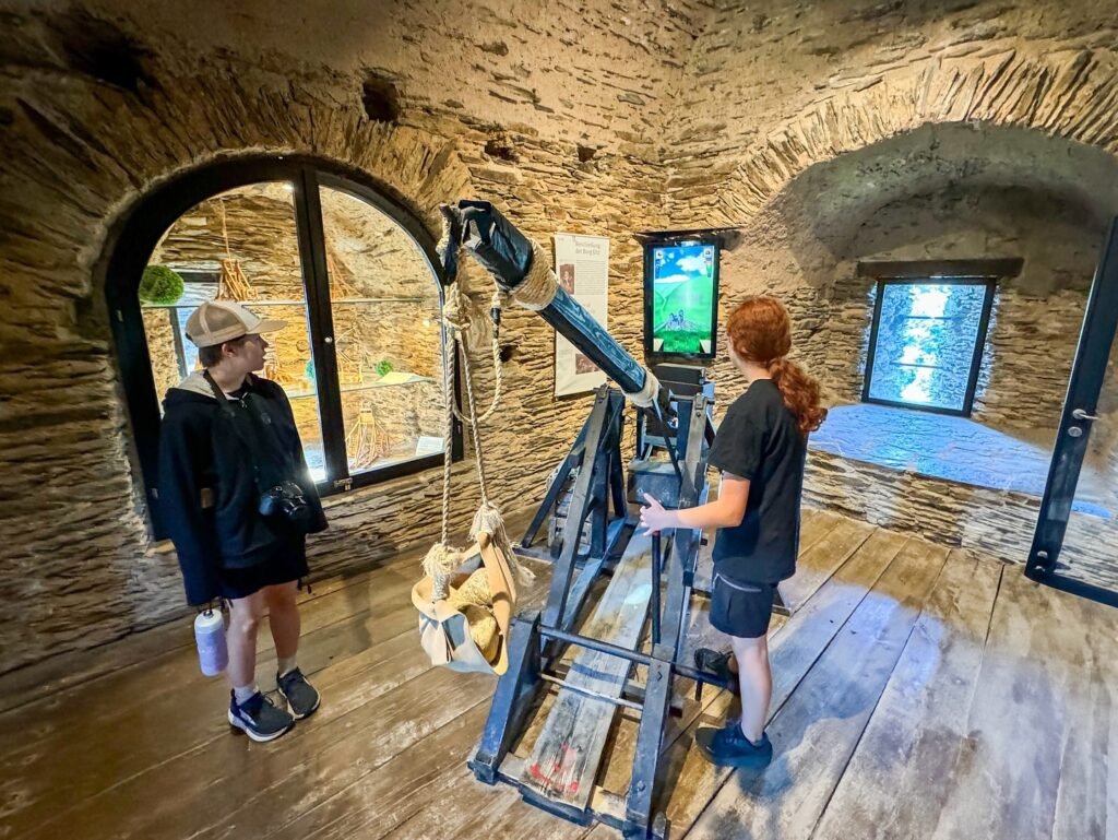Visitors examine an antique telescope and interactive display inside a historic stone structure.