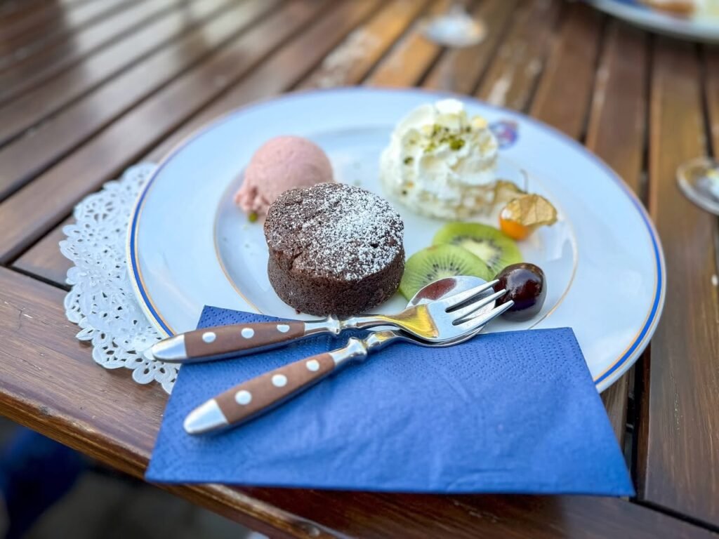 A plate of assorted desserts including a powdered cake, ice cream, and fruit, served on a wooden table with a blue napkin.