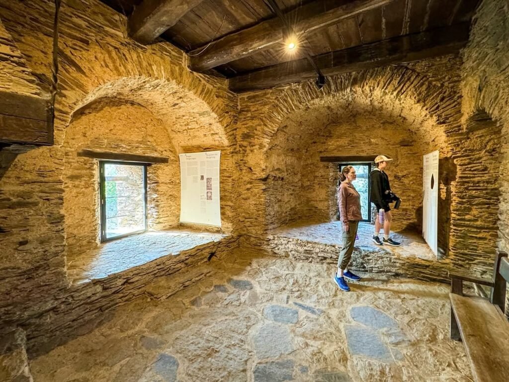 Visitors walking through a rustic stone room with arched brickwork, exposed wooden beams, and flagstone floors.