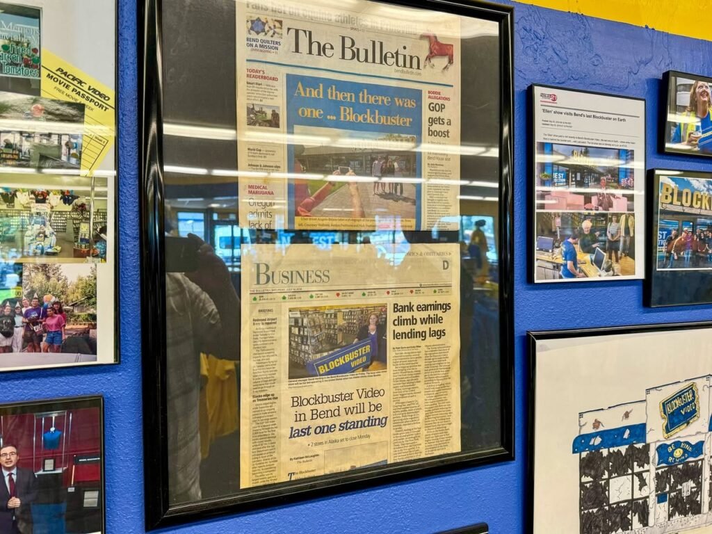 A framed edition of The Bulletin is displayed on a blue wall alongside other matted documents and photographs. The main paper shows a headline about the Blockbuster Video chain in Bend.