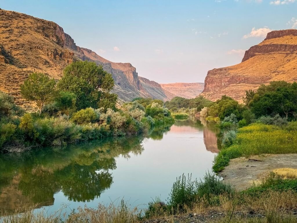 A serene river winding through a rugged landscape with tall cliffs and vibrant greenery.