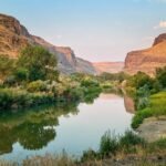 A serene river winding through a rugged landscape with tall cliffs and vibrant greenery.