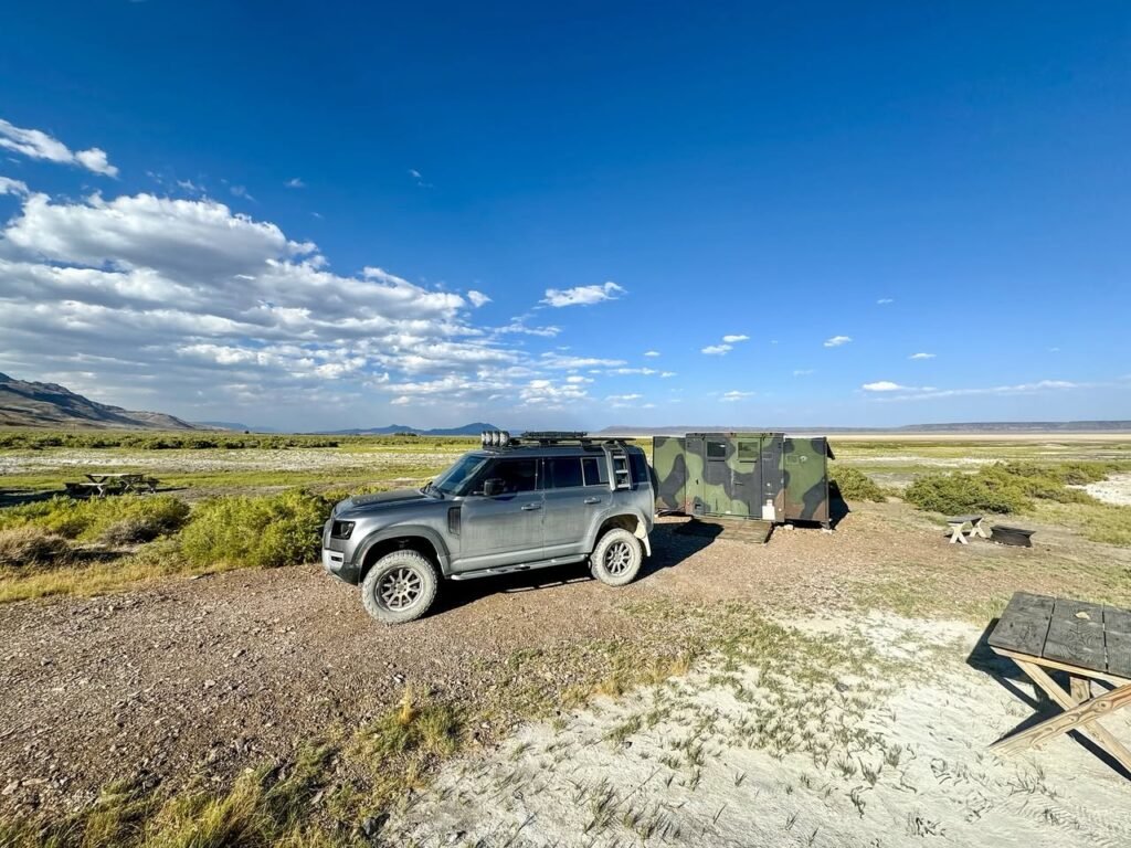 A camper pulls into a remote off-road campsite under a vast, open sky.