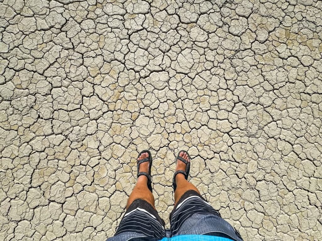 A person standing on dry, cracked earth with a close-up view of the textured soil.