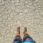 A person standing on dry, cracked earth with a close-up view of the textured soil.