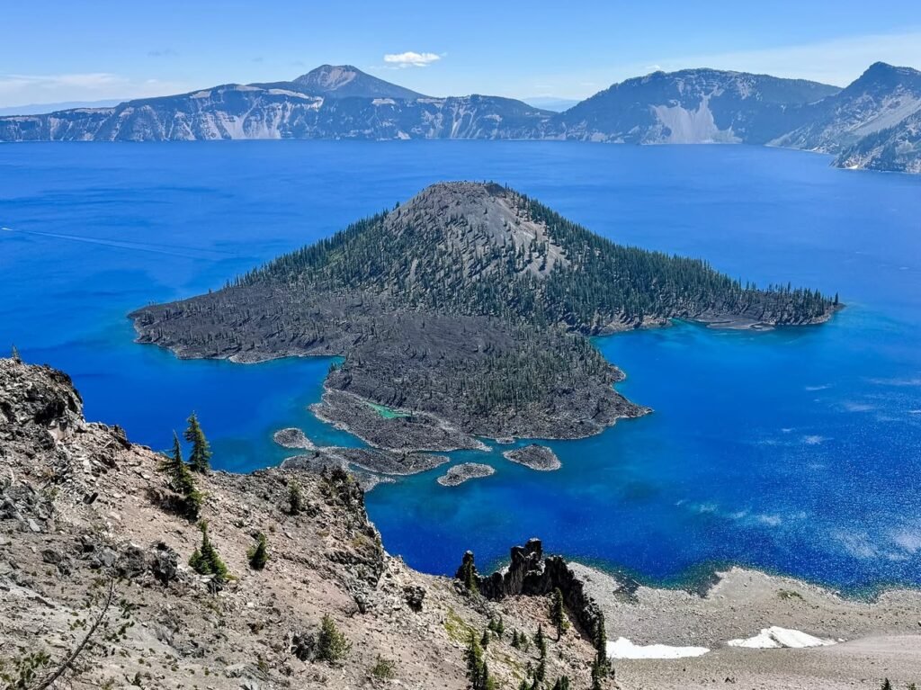 A bird's-eye view of Wizard Island in Crater Lake, showcasing its deep blue water and volcanic caldera landscape.