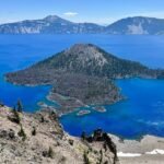 A bird's-eye view of Wizard Island in Crater Lake, showcasing its deep blue water and volcanic caldera landscape.
