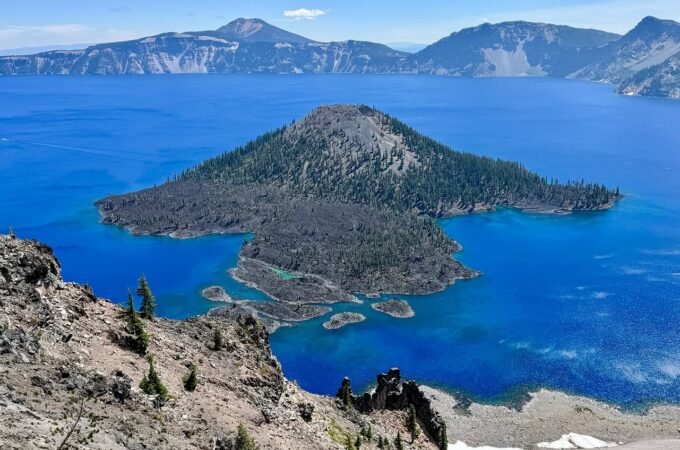 A bird's-eye view of Wizard Island in Crater Lake, showcasing its deep blue water and volcanic caldera landscape.