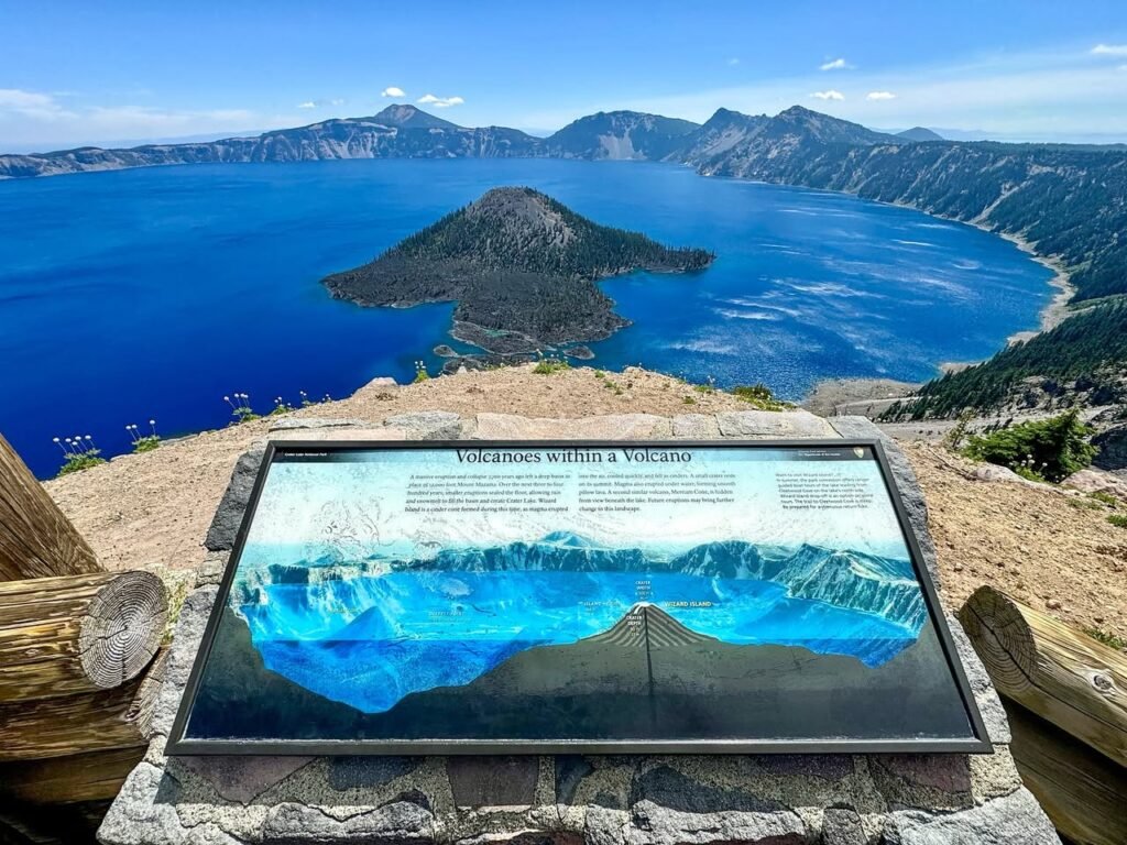 A scenic overlook at Crater Lake with an informational display panel overlooking the deep blue lake and Wizard Island.