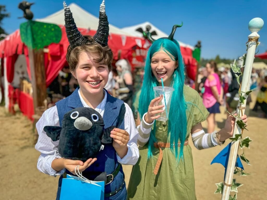 Visitors in creative cosplay at a sunny Renaissance Festival, featuring a dinosaur headpiece and teal hair.