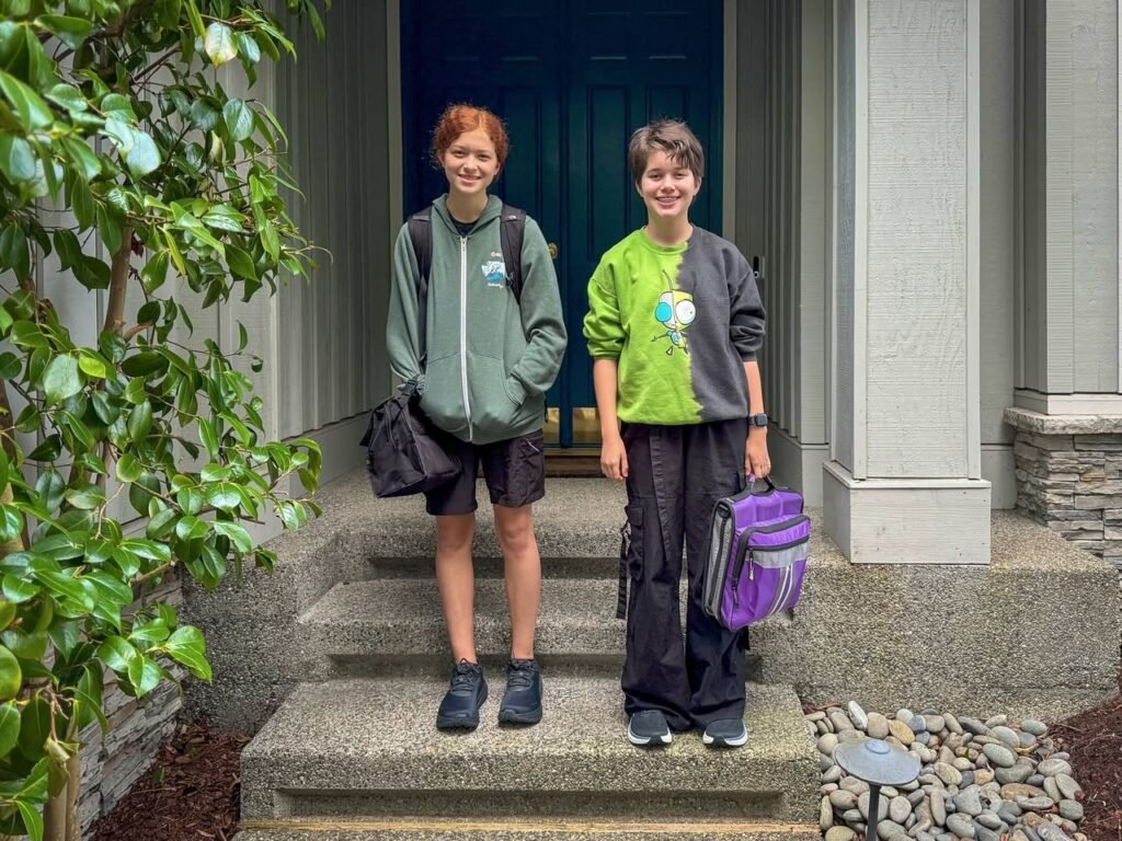 Two young people smiling on a front porch step with a purple backpack.
