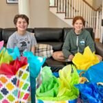 Two people sitting on a black leather sofa with colorful gift bags in the foreground.