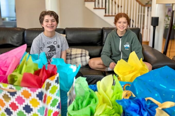 Two people sitting on a black leather sofa with colorful gift bags in the foreground.