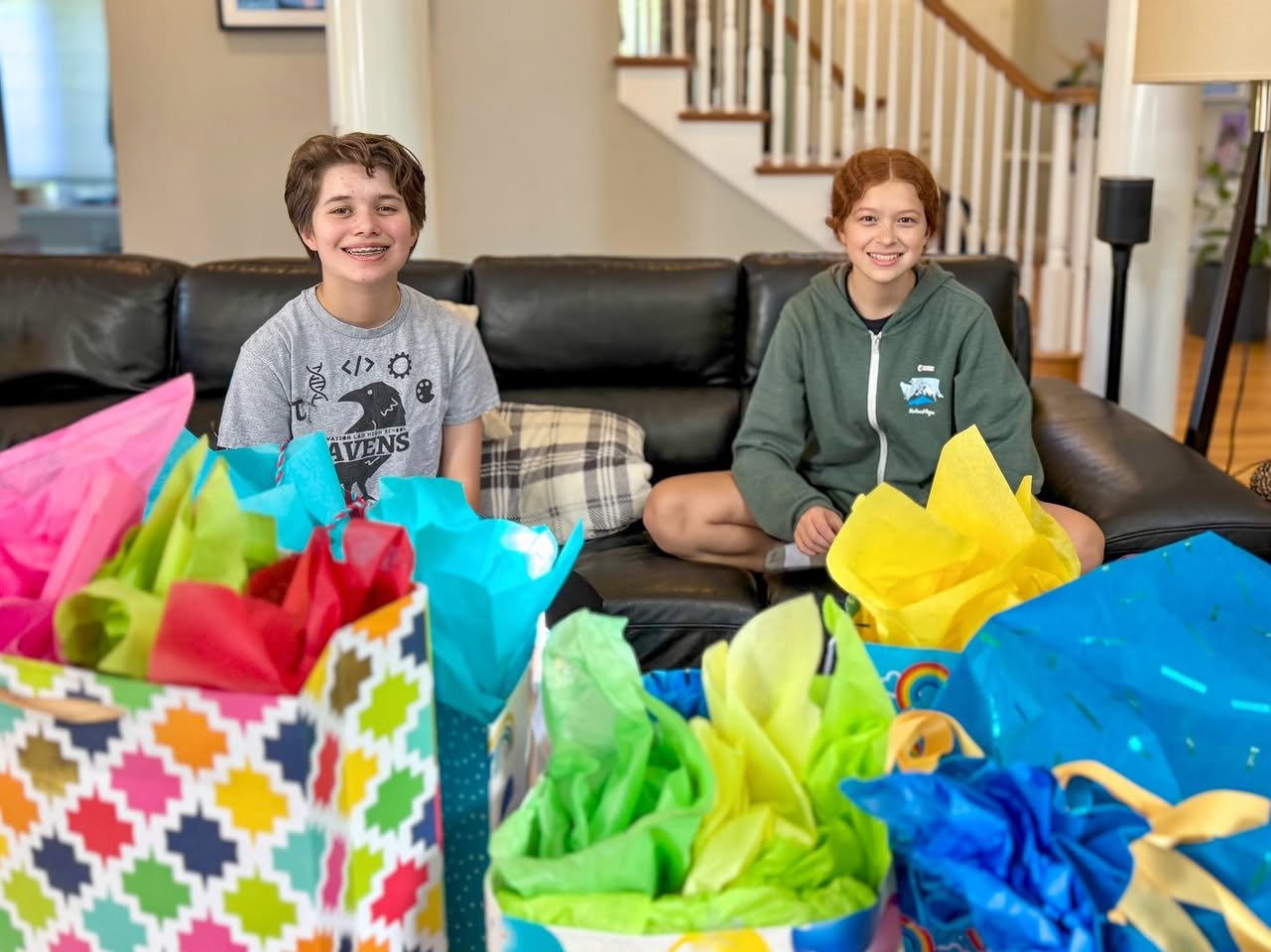 14th Birthday Two people sitting on a black leather sofa with colorful gift bags in the foreground.
