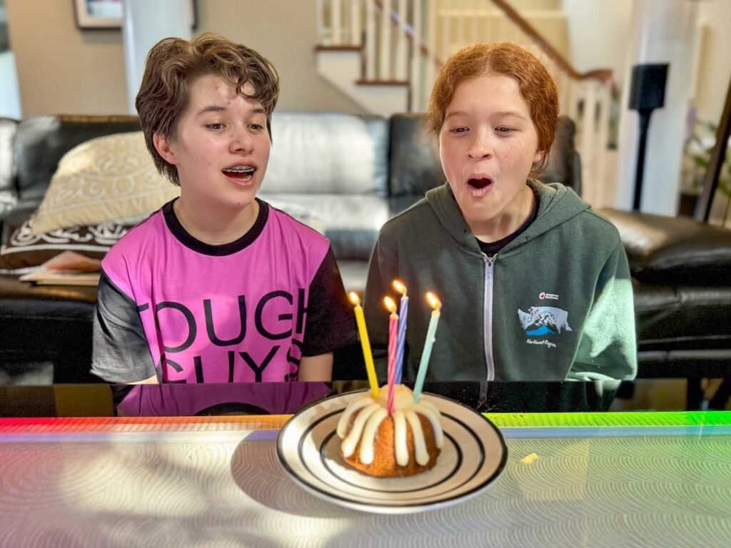 A person is seen celebrating over a birthday cake with lit candles and icing rings.