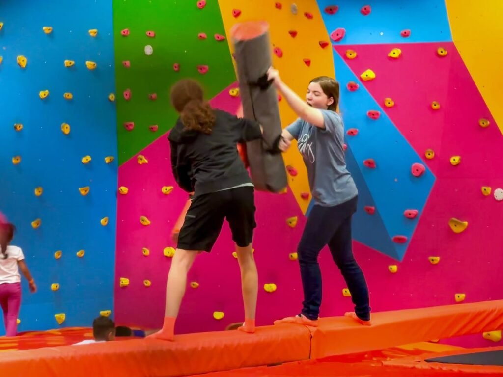People playing on colorful mats in front of bright climbing walls.
