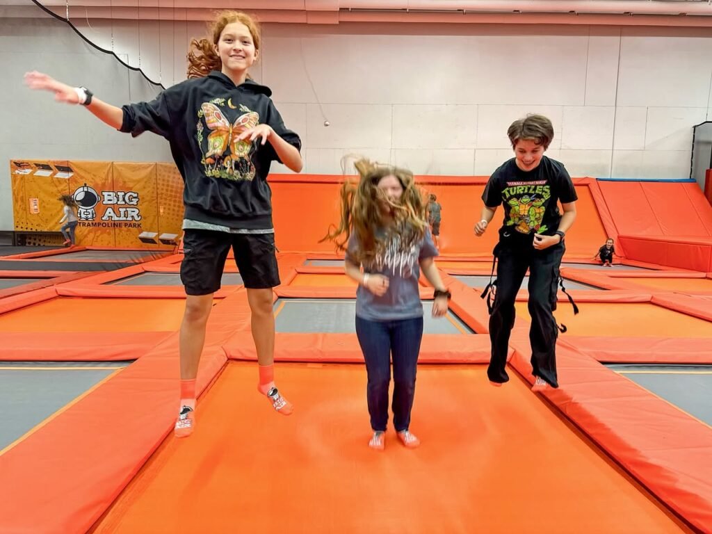 People bouncing on orange trampolines in an indoor park.