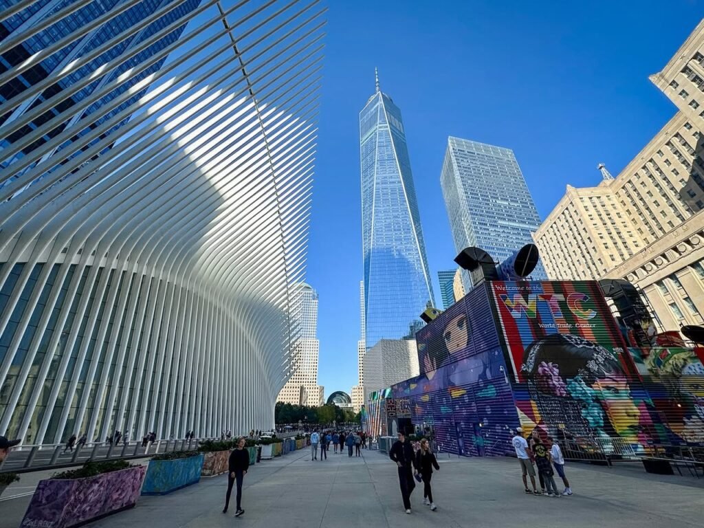 Visitors walk through the bustling Oculus terminal in New York City, with One World Trade Center towering in the background.