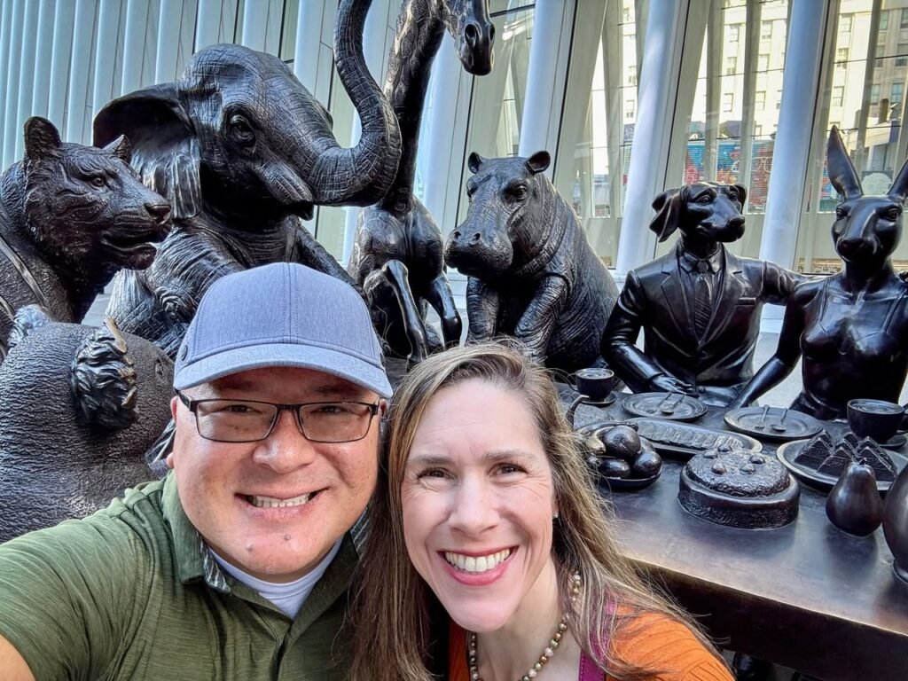 A portrait of a traveler posing with a detailed bronze statue of a dog wearing a suit, accompanied by a companion.