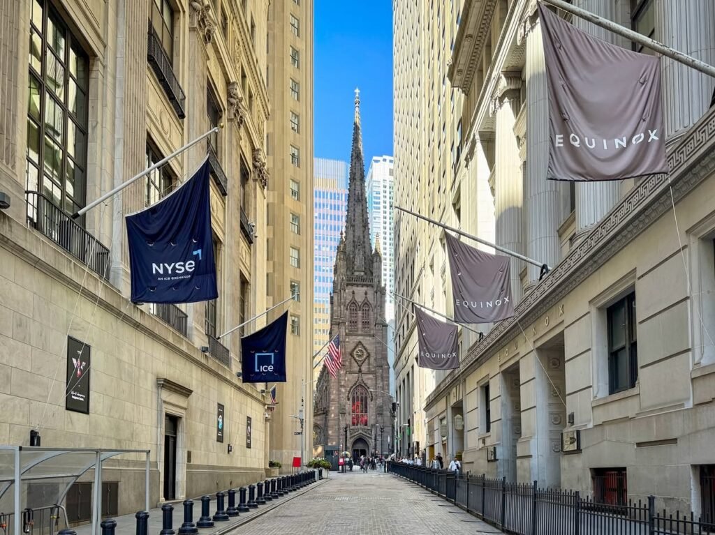 A narrow alley lined with buildings leading to a church steeple, featuring NXSE and Equinox banners.