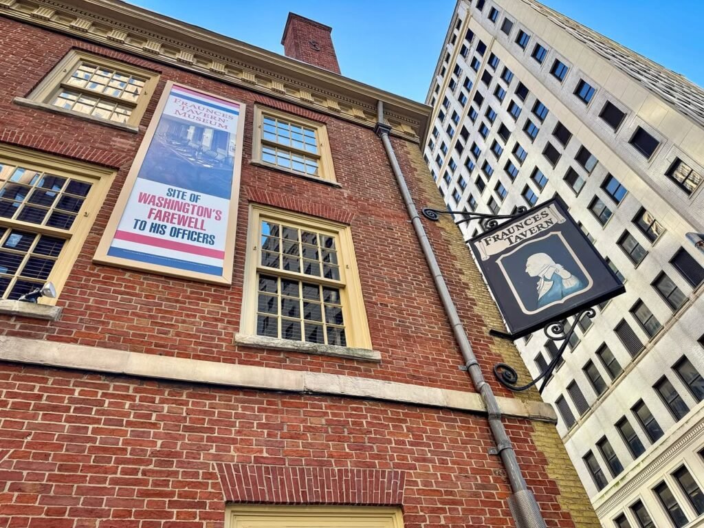 Historic red brick building with large windows and a hanging sign, set against a modern skyscraper in Boston.