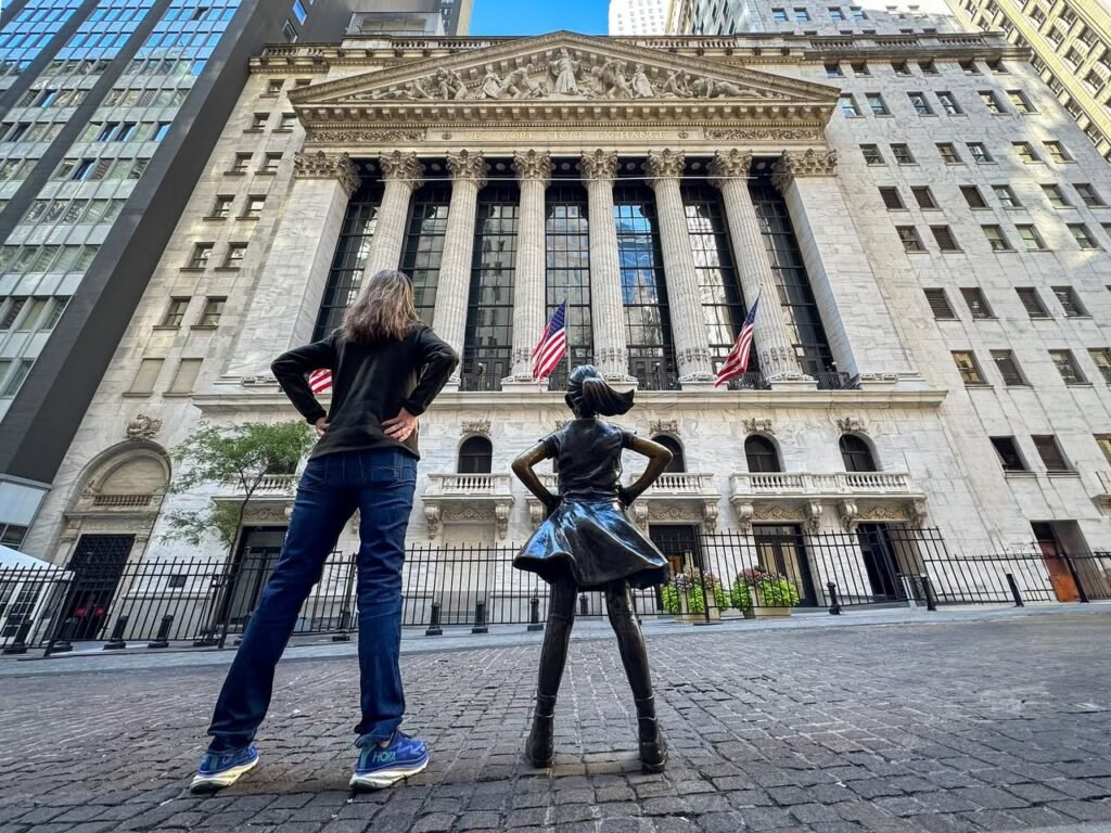 Two people posing with hands on hips in front of a historic building, one mimicking a nearby statue.