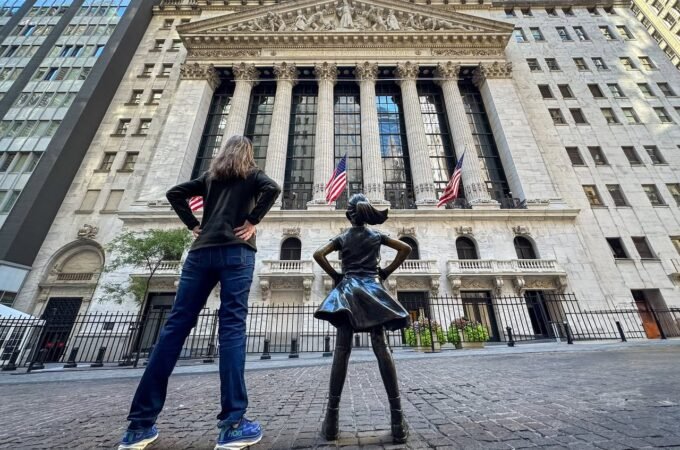 Two people posing with hands on hips in front of a historic building, one mimicking a nearby statue.