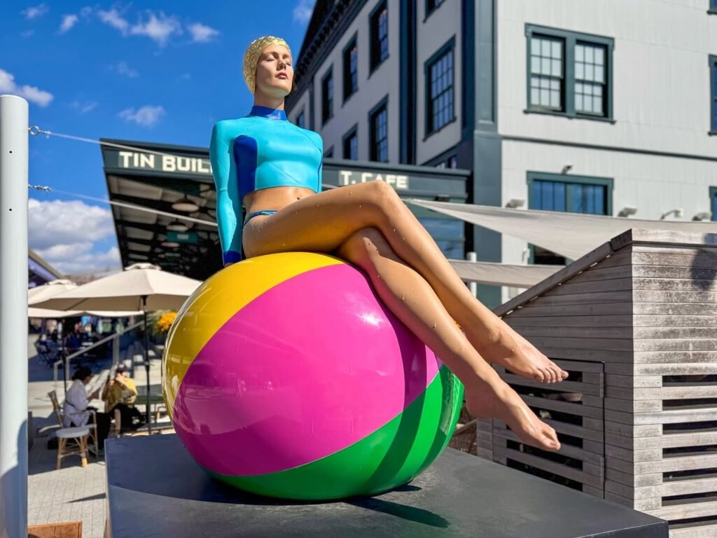 A vibrant statue of a figure seated on a large multicolored ball is displayed near the Tin Building in Seattle.