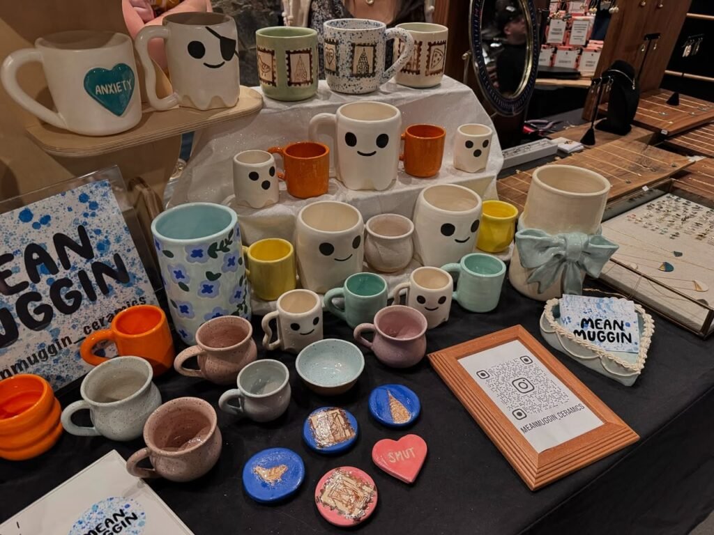 Discover a delightful collection of ceramic mugs and pottery at the Mean-Muggin vendor's booth, featuring playful designs and vibrant colors.