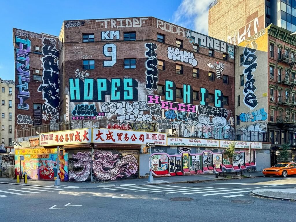 A colorful mural covers a brick building in Chinatown, New York. The artwork features varied graffiti styles and urban textures.