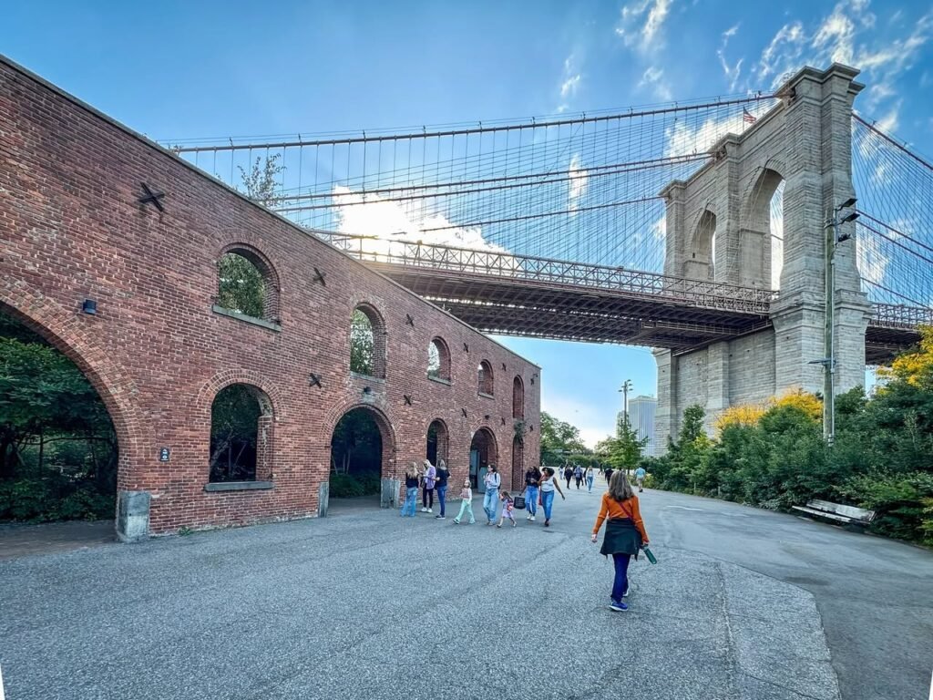 View of Brooklyn Bridge from the historic Braverman Arch, North Brother Island, with pedestrians passing by under the towering bridge.