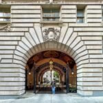 Upper West Side A grand stone archway leading into a historic building with intricate architectural details and a person walking through the passageway. The exterior facade features classical design elements and is a popular subject for urban photography enthusiasts.