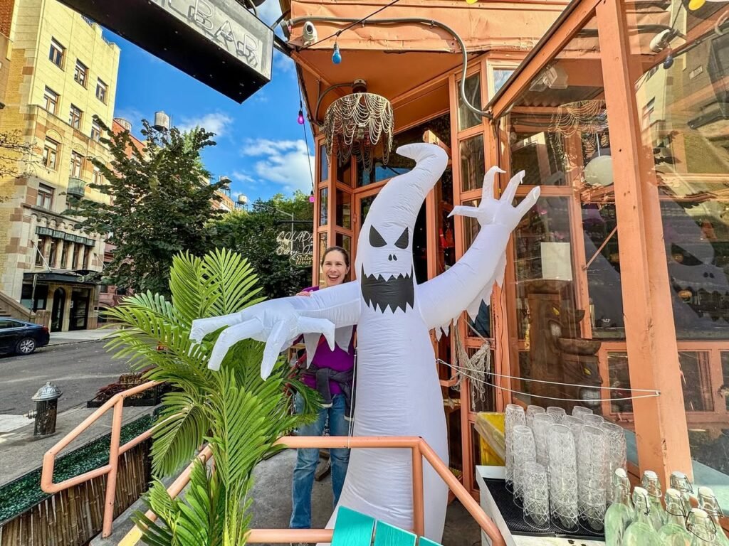 A person wearing a tall, inflatable white ghost costume with an angry face, standing on a city sidewalk.