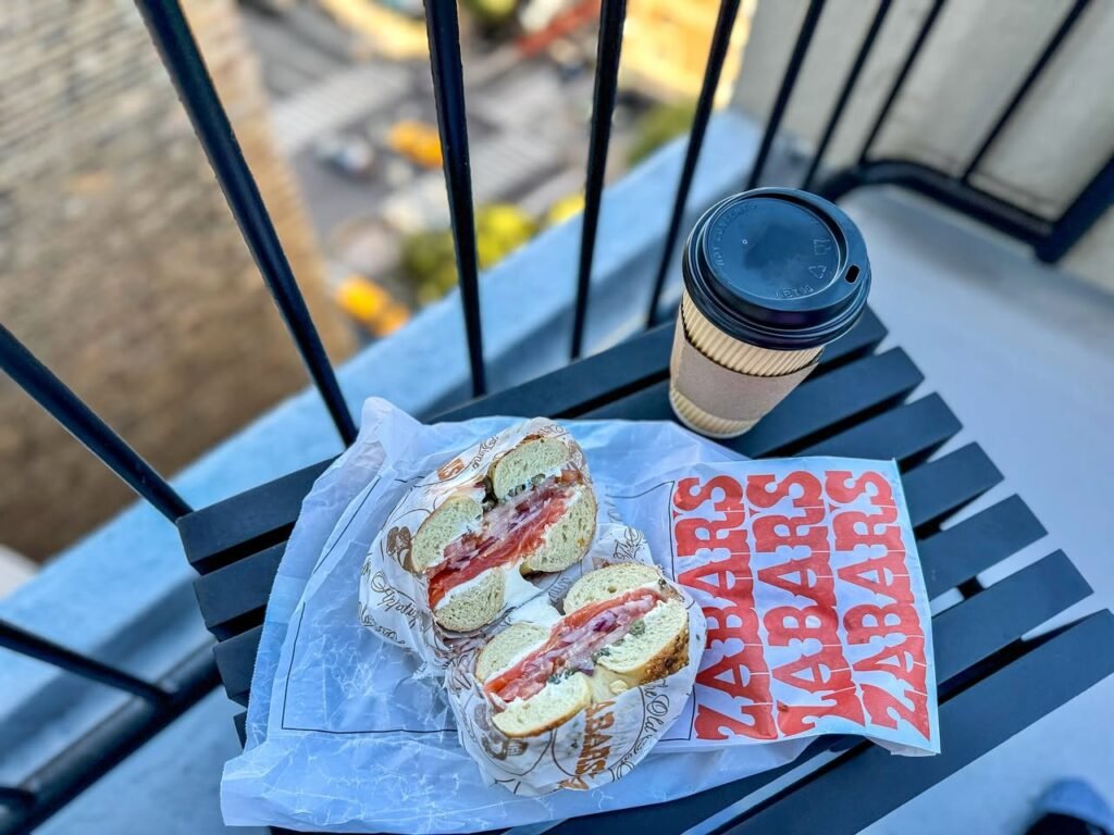 A breakfast bagel sandwich from Zabars and a coffee cup sit on a patio chair. The fresh breakfast is ready to enjoy while traveling.