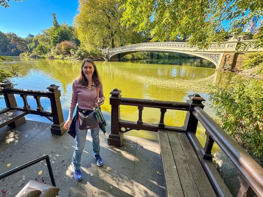 Standalone views of a stone arch bridge over a calm lake and a person on a wooden deck. A stone bridge curves gracefully over a green-tinged lake, framed by lush autumn trees.