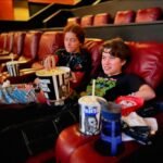 Enjoying popcorn and drinks while seated in an indoor movie theater.