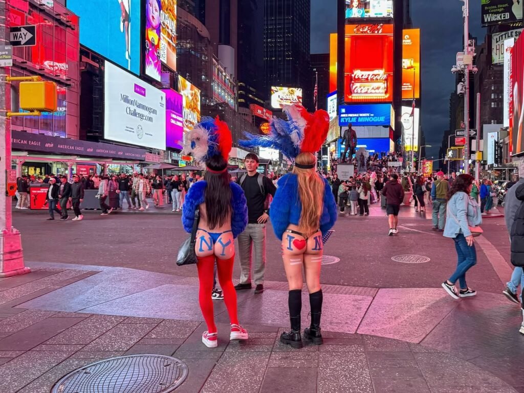 Two costumed performers stand in Times Square with vibrant billboards and pedestrians in the background.