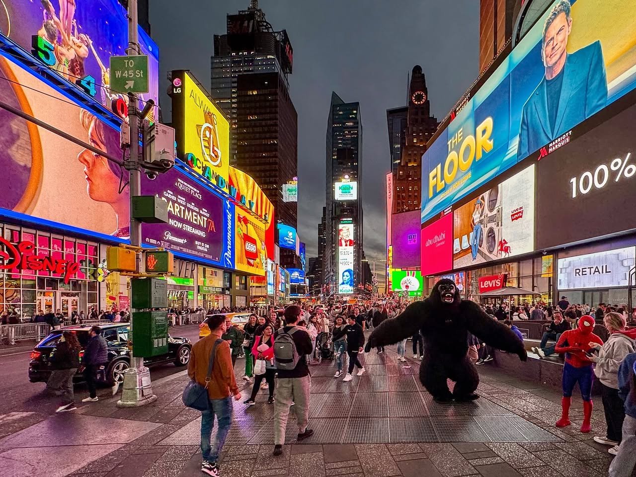 Olive Garden Times Square A bustling street scene in Times Square, New York City, featuring bright digital billboards and costumed performers.