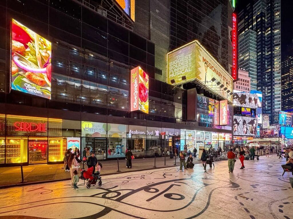 Optical illusion paintings on the wet pavement of New York City's Times Square at night, surrounded by vibrant neon lights and crowds.
