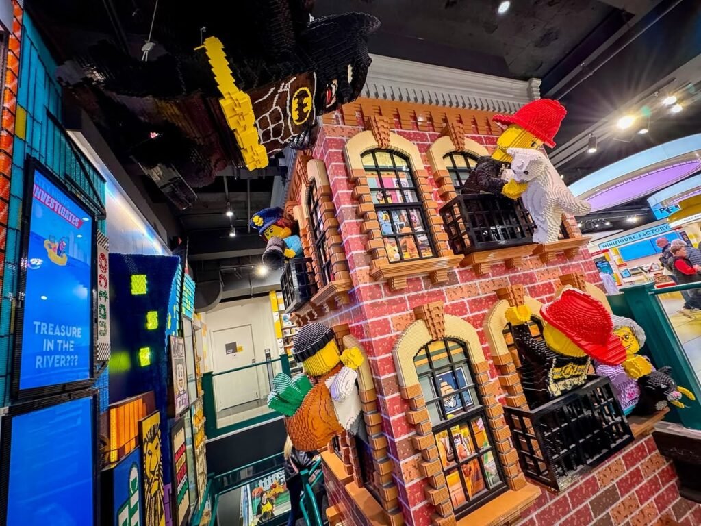 A colorful display of a large Lego brick building with minifigure characters in an indoor museum setting.