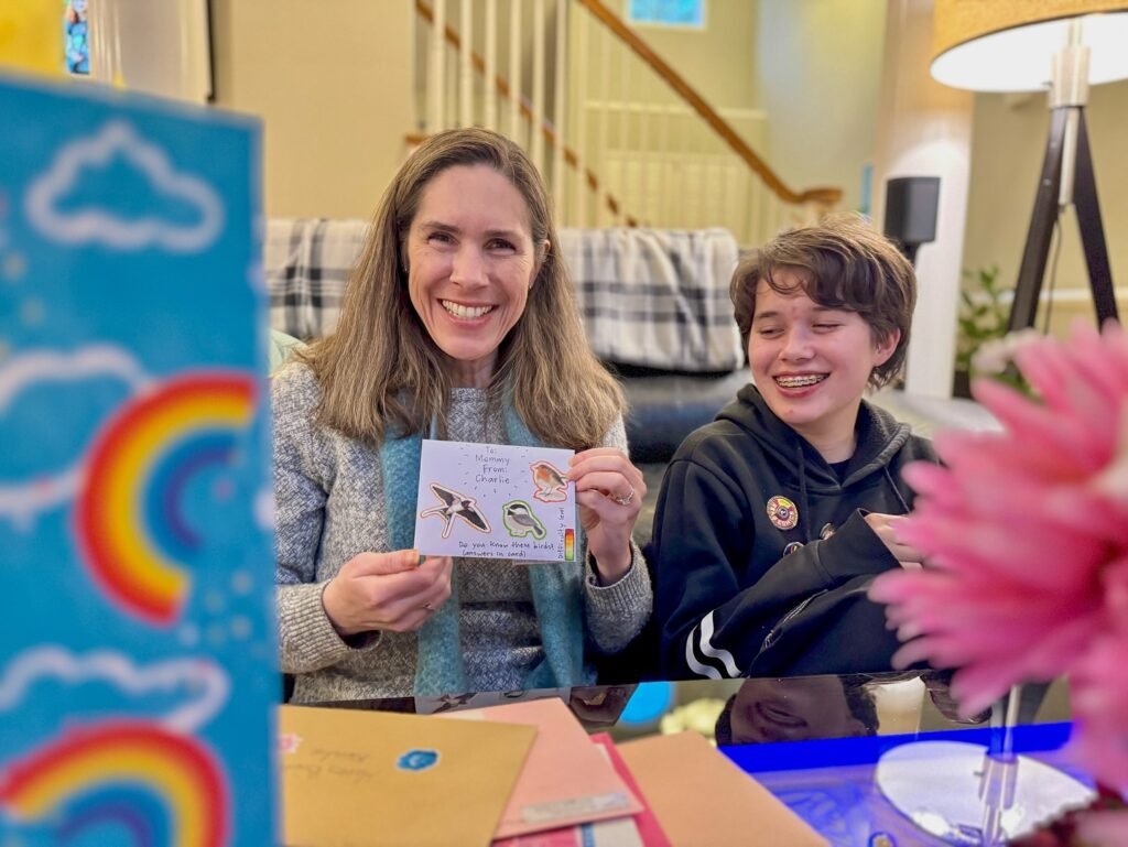 A smiling woman and child share a postcard together in a cozy living room.