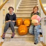 Chelan Valley Farms Two young people pose with glowing carved pumpkins on a staircase in a home.