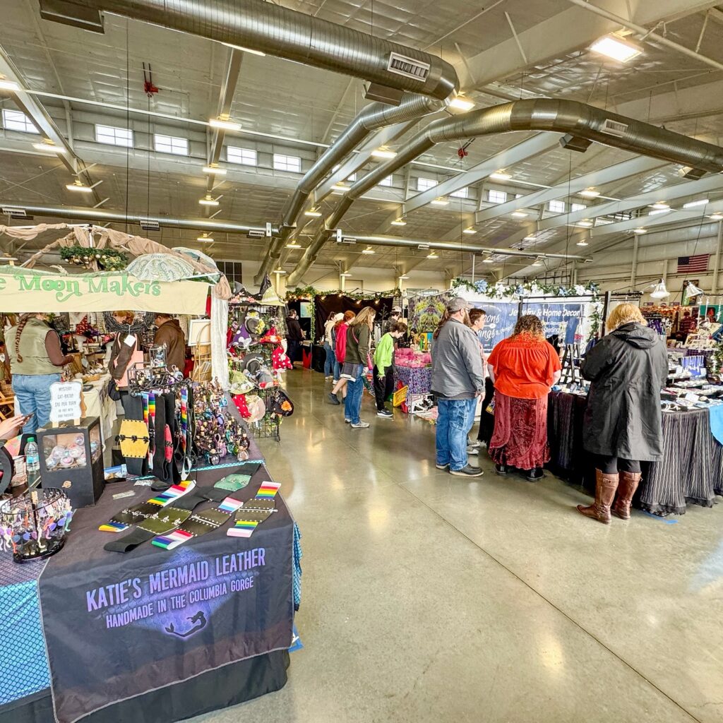 An indoor craft fair featuring various vendor booths in a spacious hall with a high ceiling.