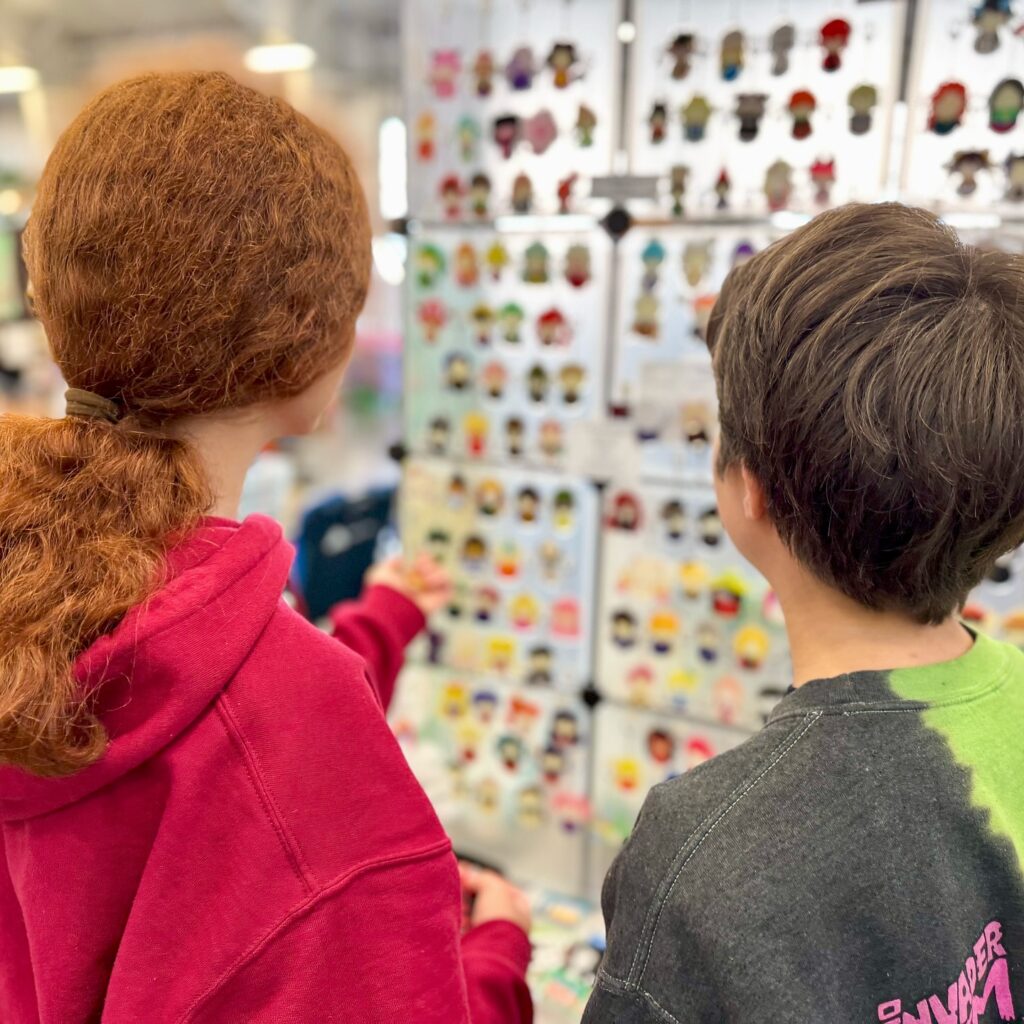 Two people browsing a large display board filled with colorful and personalized pet tags at a retail store.