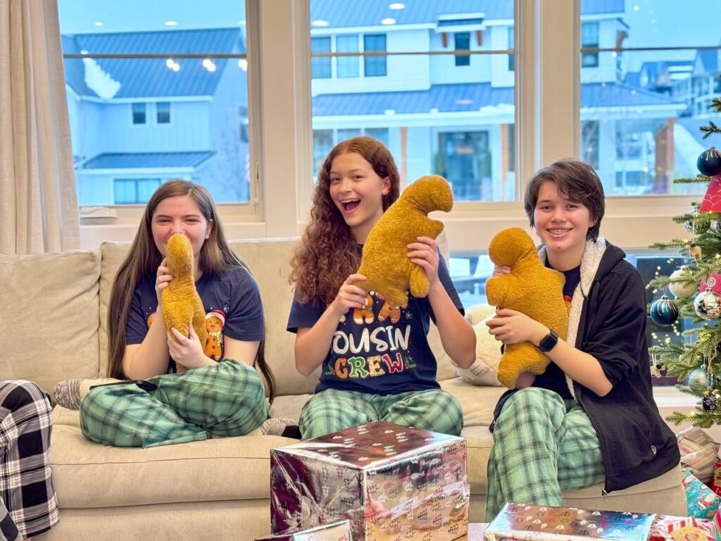 Three people enjoying a cheery holiday morning with golden retriever plushies and wrapped gifts on the couch.