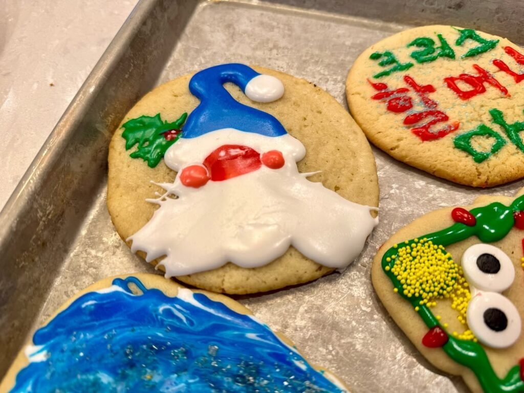 Christmas cookies decorated with Santa, a tree, a snow globe, and 'Happy Holidays' text on a baking sheet.