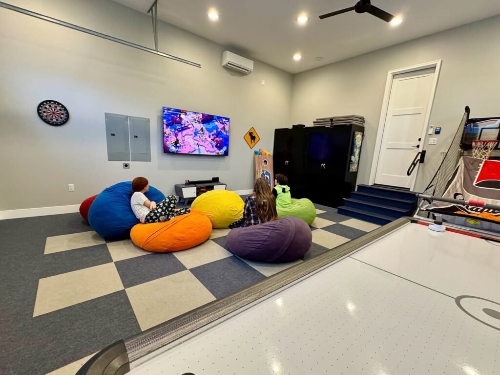 A cozy gaming lounge featuring a black-and-white checkered floor, colorful bean bag chairs, and various coin-operated arcade games.