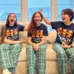 Snowboard Lessons Three kids wearing matching gingerbread Christmas pajamas sit on a couch, laughing and having fun near a decorated holiday tree.